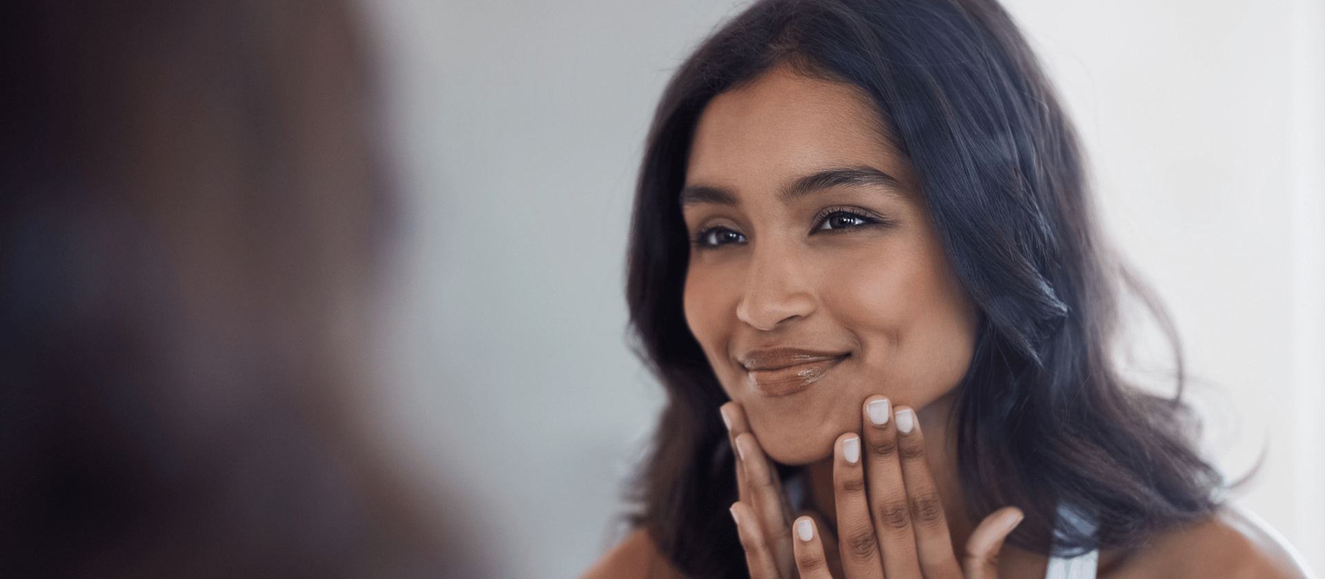 woman with glowing skin smiling at self in mirror